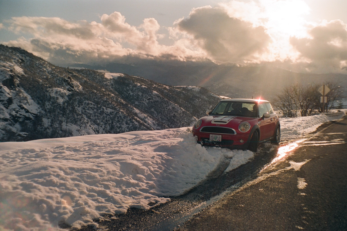 A photo of a red mini cooper on a snowy mountain road