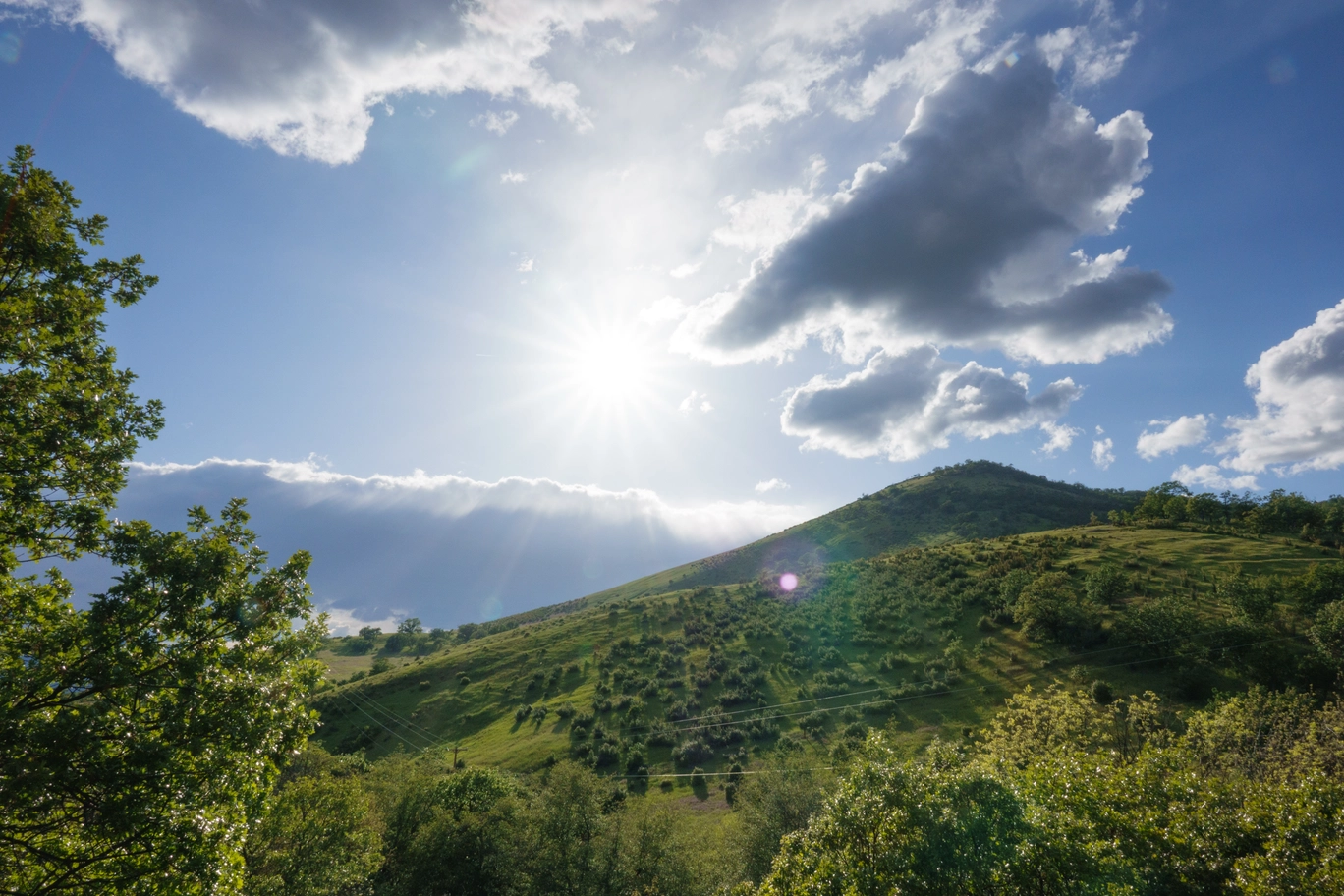 A photo of green hills and the sun