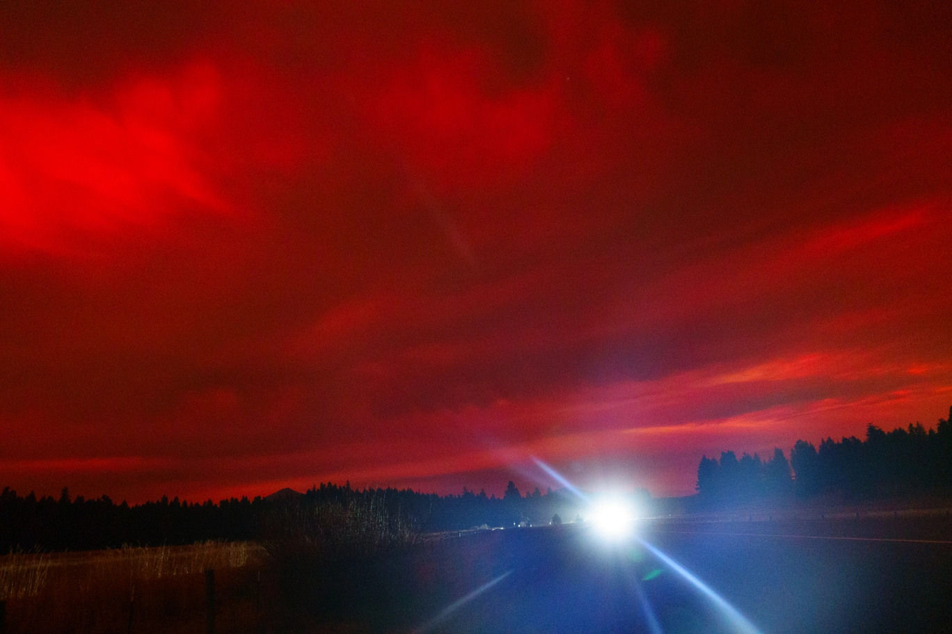 A photo of car headlights and red clouds covering the sky at night due to the Aurora Borealis