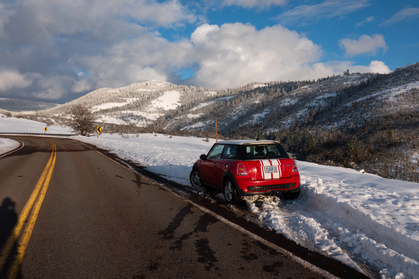 A photo of a red mini cooper on a snowy mountain road
