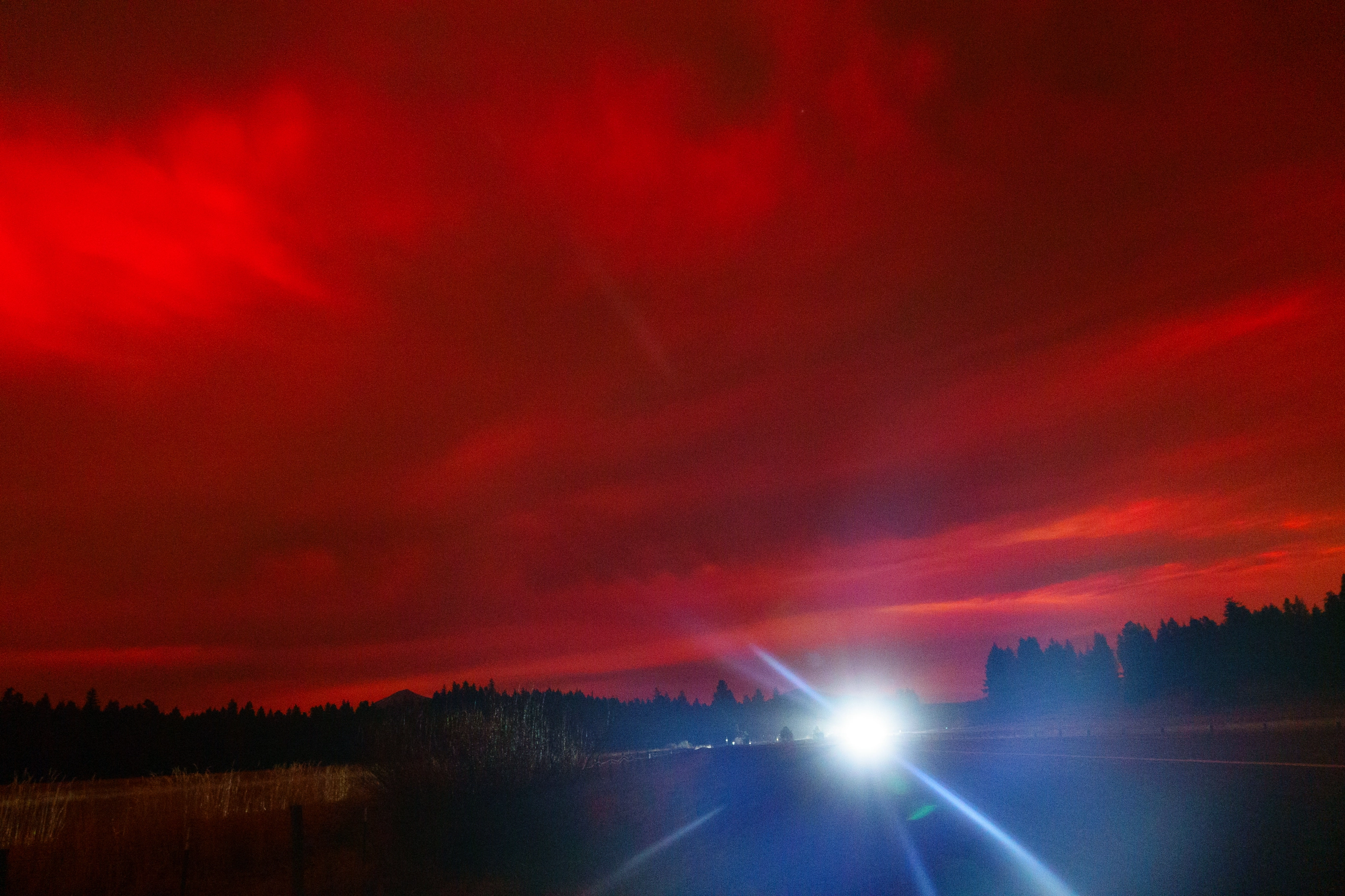 A photos of car headlights and red clouds covering the sky at night due to the Aurora Borealis
