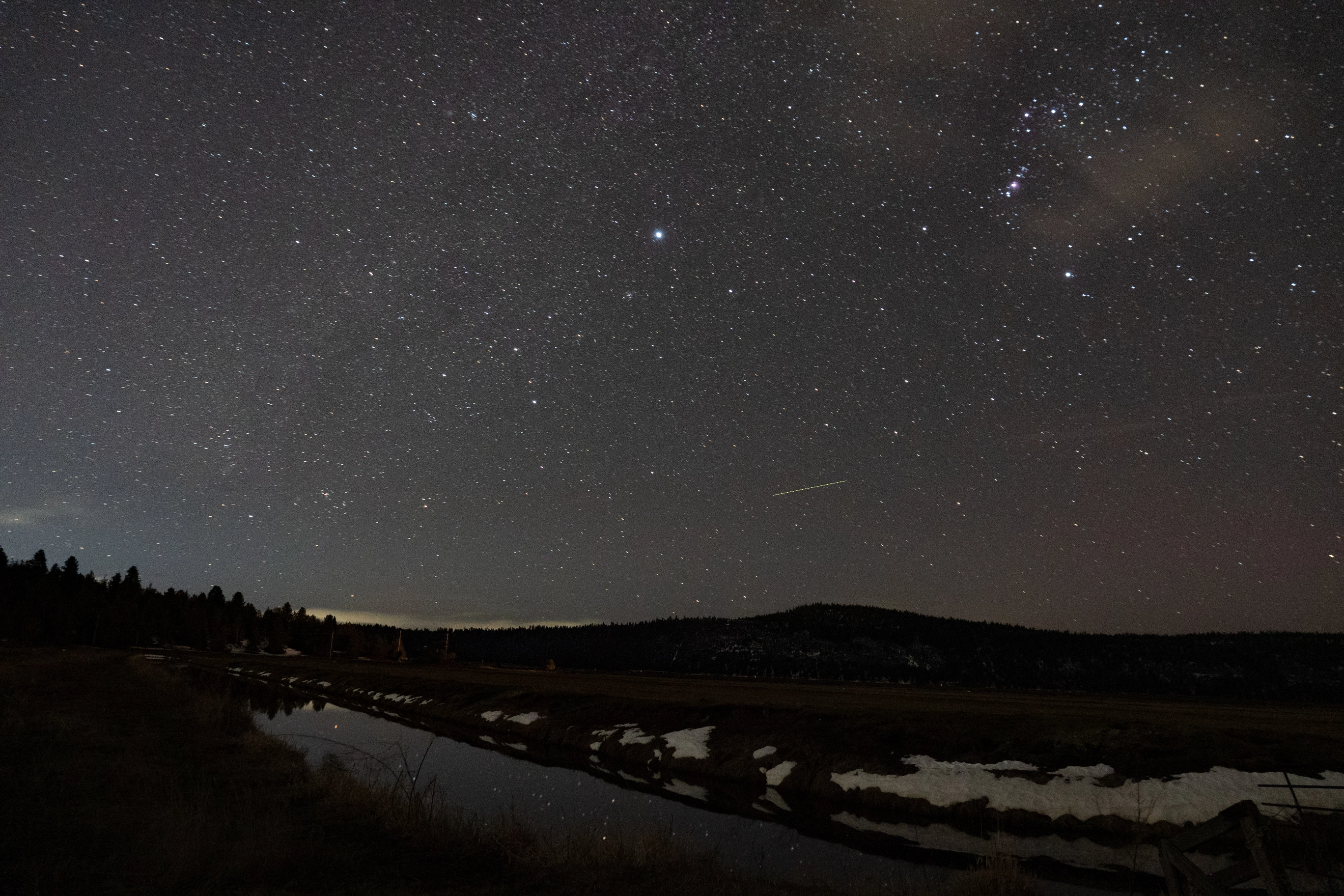 A photo of the night sky with some mountains and fields in the foreground